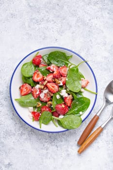 Light Healthy Summer Salad with fresh Strawberries, Spinach, Cream Cheese and Walnuts on White Ceramic Plate, white rustic stone Background Top View.