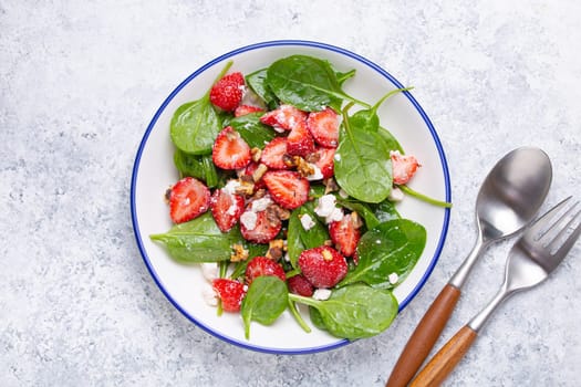 Light Healthy Summer Salad with fresh Strawberries, Spinach, Cream Cheese and Walnuts on White Ceramic Plate, white rustic stone Background Top View.