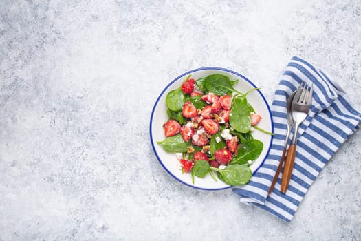 Light Healthy Summer Salad with fresh Strawberries, Spinach, Cream Cheese and Walnuts on White Ceramic Plate, white rustic stone Background From Above, Space For Text.