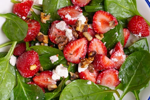 Close Up of Light Healthy Summer Salad with fresh Strawberries, Spinach, Cream Cheese and Walnuts on White Ceramic Plate, white rustic stone Background Top View.