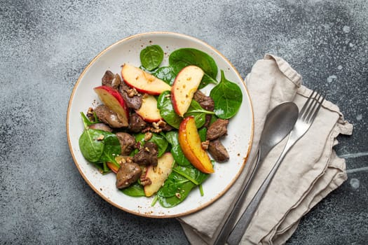 Healthy Salad with Iron Rich Ingredients Chicken Liver, Apples, Fresh Spinach and Walnuts on White Ceramic Plate, Grey Rustic Stone Background Top View.