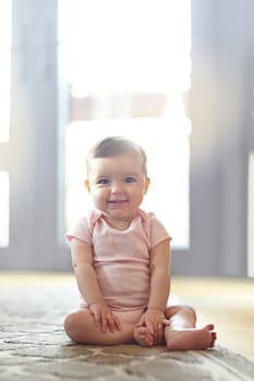 Shes got some mischief in her eyes. Portrait of an adorable baby girl sitting on the living room floor