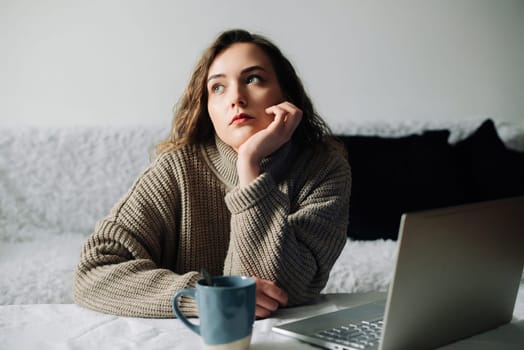 Creative woman working from home writing lesson plan and schedule for students, using laptop and sipping coffee at kitchen table. Productive teacher writes outline and schedule at laptop.
