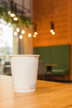 Takeaway coffee. Paper cup of coffee on wooden table in cafe blur background. Hot coffee . Copy space for text. Selective focus. The atmosphere is warm coffee shop. Drinking concept.