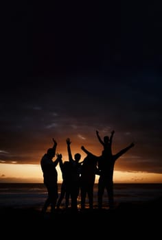 Carefree, sunset and silhouette of friends at the beach while on a summer vacation, adventure or weekend trip. Freedom, happy and shadow of group of people having fun together by the ocean on holiday.