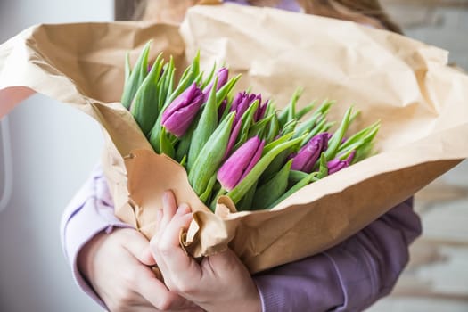 Hands wrapping purple tulips bouquet in craft paper overwooden table top view. Rustic valentines gift