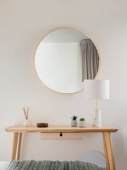 Close-up of a wooden table and a frame with mirror with stylish accessories in a young womans bedroom. The concept of stylish minimalist interior design in a new apartment. Copyspace.