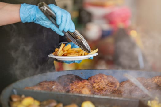 Fast food restaurant on the street. A female chef uses tongs to place crispy fried potatoes on a plate for a customer. Cooking in a fast food restaurant. High quality photo