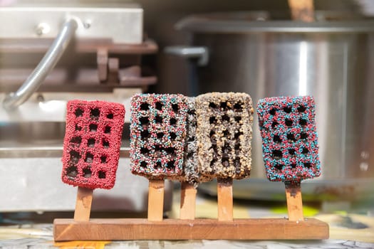 Belgian waffles on a wooden stick covered with chocolate icing. Production and sale of fresh Belgian waffles in a pastry shop. High quality photo