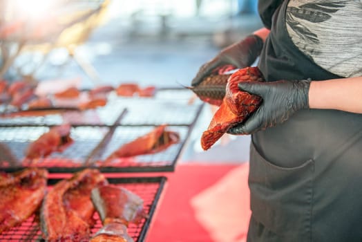 The process of smoking sea bass. A woman in a fish smoking factory lays out sea bass for smoking on a grill. The concept of the fishing industry. High quality photo