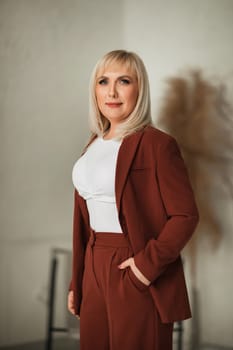 A fashionable woman with makeup in a teracote suit poses in the interior.