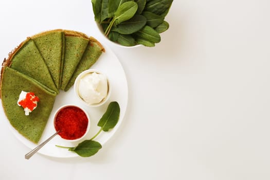 Spinach pancakes on a plate with soft cheese and caviar on a white background. copy space