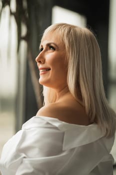 A fashionable woman in a white shirt poses in the interior.