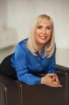 A fashionable woman in a blue shirt and black trousers poses in the interior.