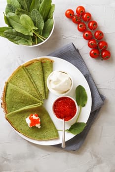 Spinach pancakes on a plate with soft cheese, caviar and cherry tomatoes on a gray background with textile. vertical photo