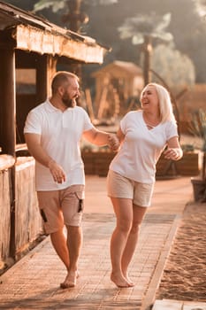 A happy married couple in shorts and T-shirts walks down the street at sunset in summer.