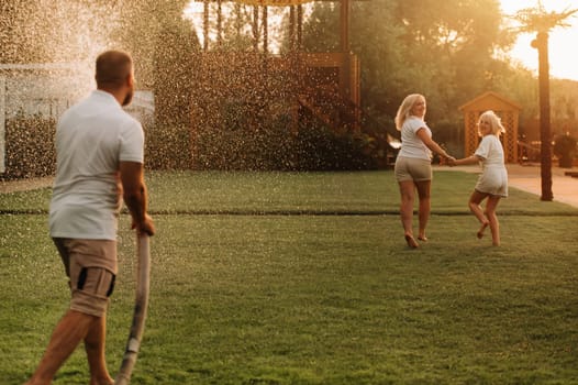 A man pours water from a hose on his wife and daughter on the lawn.