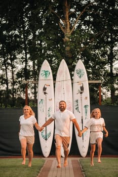 A family of three stands against a backdrop of surfboards at sunset.