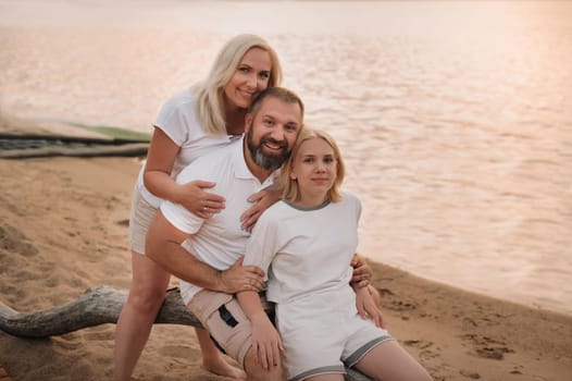 Happy family of three relaxing sitting on the beach after sunset.