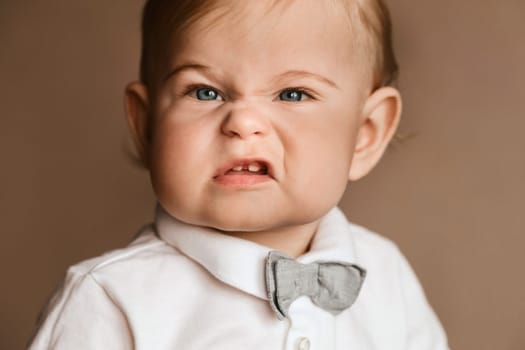 Portrait of a little boy in a white shirt with a bow tie grimacing on camera.