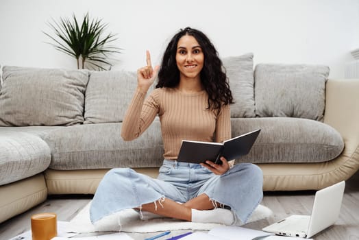 Young beautiful Hispanic woman has a good idea about planning his work. The girl sits on the floor and holds a notebook. Freelancing is an opportunity to work from home.