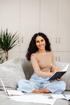 Head shot smiling woman taking notes watching webinar, studying online at home, happy young female listening to lecture, engaged in internet educational course, remote education.