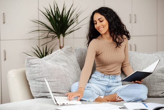 Distance Education. Portrait of smiling woman sitting on sofa, using laptop and writing in notebook, taking notes, watching tutorial, lecture or webinar, studying online at home looking at screen
