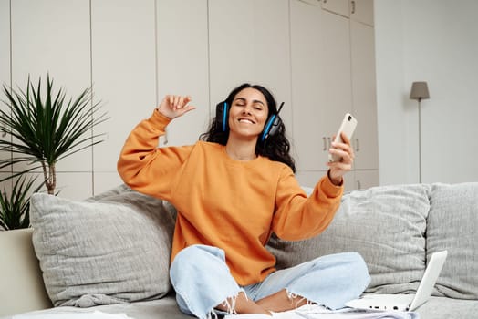 A young beautiful girl of Arab appearance sits on a sofa in a homely atmosphere. The girl dances and listens to music in headphones enjoys a break in the working moment.