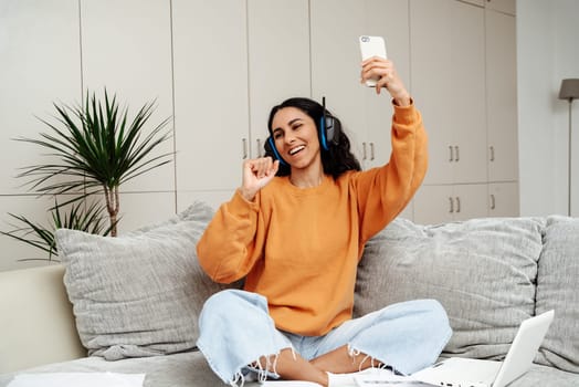 Funky teenage girl singing favorite song, listening to music podcast on headphones using app at home, happy funny young woman in headset enjoying new audio tracks playing on digital app.