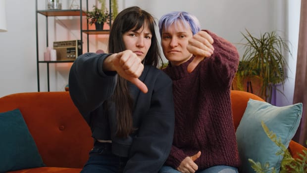 Dislike. Upset two lesbian women family couple or girls friends showing thumbs down sign gesture, expressing discontent, disapproval, dissatisfied bad work at home living room. Displeased LGBT people