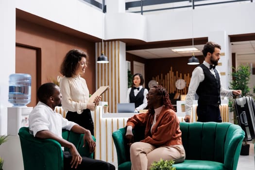 Woman welcoming hotel guests in lobby, providing excellent luxury service to people at resort. Young manager discussing about staff and accommodation with tourists, giving advice.