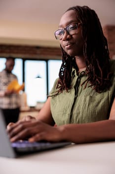 Portrait of focused student doing homework typing on laptop keyboard while colleague is reading a book in home living room. Casual african american entrepreneur working remote using portable computer.