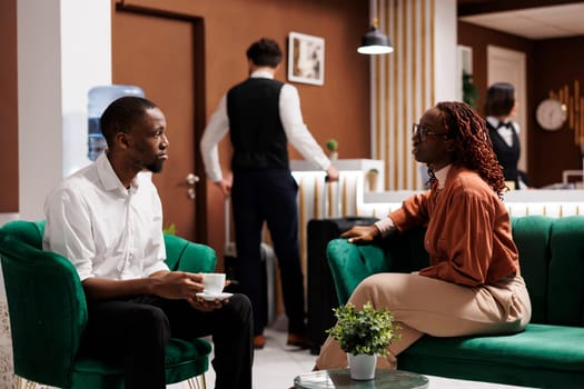 Young partners waiting in lounge area at luxury hotel, sitting together before filling in registration forms at front desk. Travelling couple with room reservation at expensive resort.