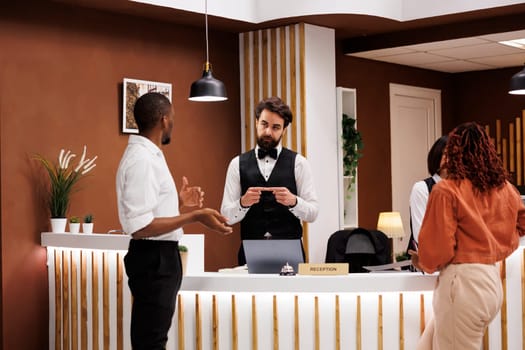 Hotel staff providing luxury service to people waiting at front desk in lobby, talking about room reservation before check in process. Young employee welcoming guests at resort.