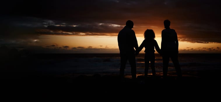 Beach, sunset and silhouette of a family holding hands in the dark while on summer vacation or trip. Adventure, love and shadow of people in nature by ocean together while on seaside travel holiday
