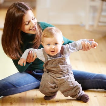 Wow, this walking thing is hard. Smiling young mom helping her baby boy learn to walk