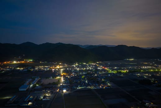 Lights from houses and streets in small town at foot of mountain range at twilight. High quality photo