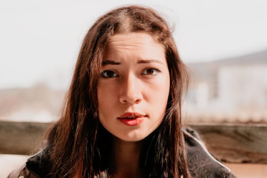 Happy young smiling woman with freckles outdoors portrait. Soft sunny colors. Outdoor close-up portrait of a young brunette woman and looking to the camera, posing against nature background.