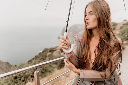 Woman rain park. Happy woman portrait wearing a raincoat with transparent umbrella outdoors on rainy day in park near sea. Girl on the nature on rainy overcast day