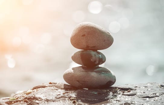 Balanced Pebbles Pyramid on the Beach on Sunny Day and Clear Sky at Sunset. Blue Sea on Background Selective focus, zen stones on sea beach, meditation, spa, harmony, calm, balance concept.