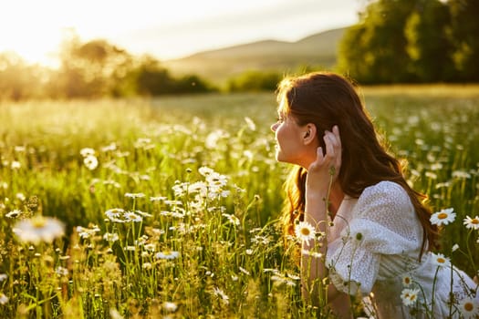 portrait of a beautiful, red-haired girl sitting in a chamomile field and looking at the sunset. High quality photo