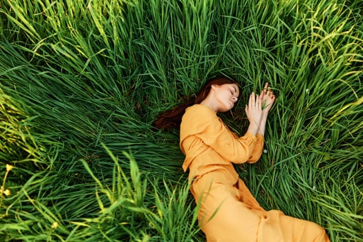 a relaxed woman enjoys summer lying in the tall green grass with her eyes closed. Photo taken from above. High quality photo