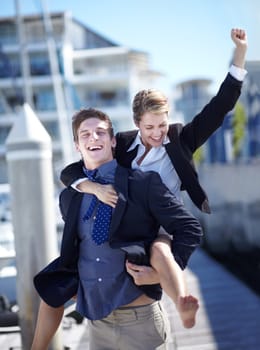 Celebration, piggyback and corporate couple at harbor excited for success, startup or travel freedom. Business people, victory and man with woman before traveling in Amsterdam, winning and hand sign.