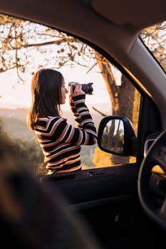 young caucasian woman taking photos of nature with a camera during a road trip in camper van, concept of van life and travel adventures