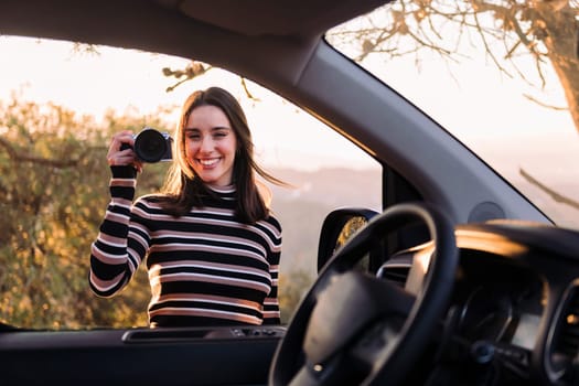 young caucasian woman smiling happy looking at camera showing a photo camera during a road trip in camper van, concept of van life and travel adventures