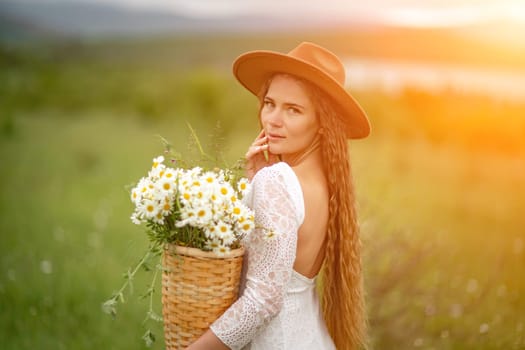 A middle-aged woman in a white dress and brown hat stands on a green field and holds a basket in her hands with a large bouquet of daisies. In the background there are mountains and a lake