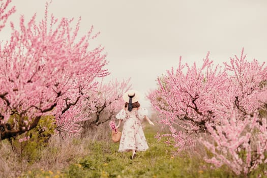 Woman blooming peach orchard. Against the backdrop of a picturesque peach orchard, a woman in a long dress and hat enjoys a peaceful walk in the park, surrounded by the beauty of nature