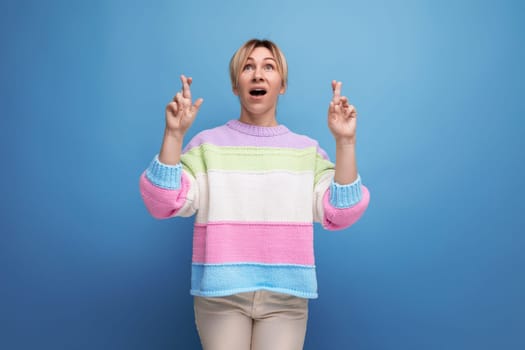 surprised blond woman in casual outfit showing hands up on blue background with copy space.