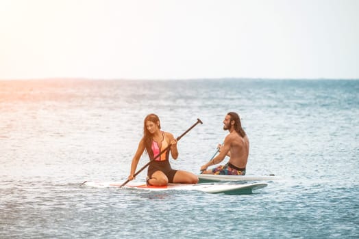 Sea woman and man on sup. Silhouette of happy young woman and man, surfing on SUP board, confident paddling through water surface. Idyllic sunset. Active lifestyle at sea or river