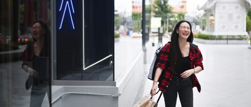 Cheerful Asian woman holding shopping bags and walking in the city street.